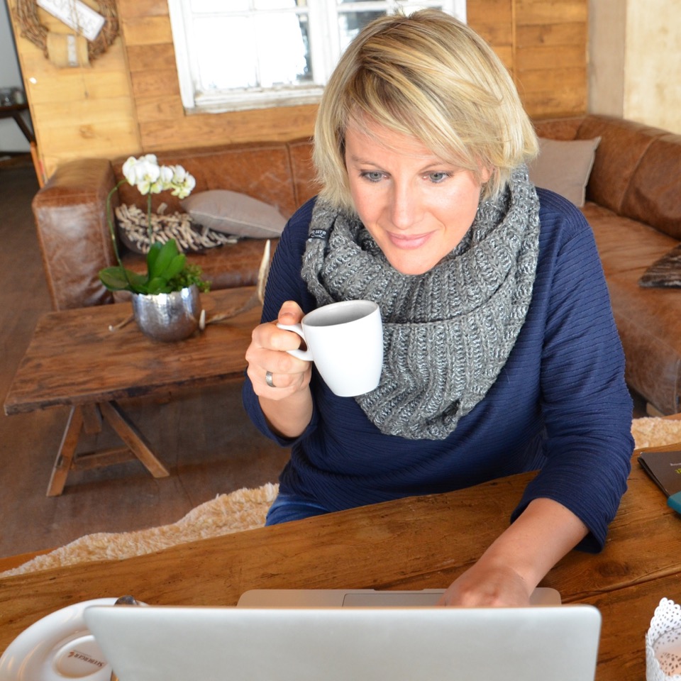 Katja Voigt sitzt am Laptop bei der Vorbereitung einer Präsentation und trinkt eine Tasse Kaffee.